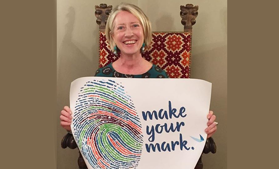 bluebird bio's first European employee sitting in a chair holding a sign that says 'make your mark'