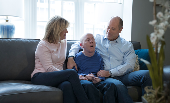 Picture of a mother and father seated on either side of their son with cerebral adrenoleukodystrophy